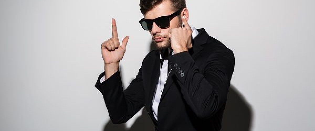 Portrait of a serious man in earphones and sunglasses showing gun gesture isolated over gray background